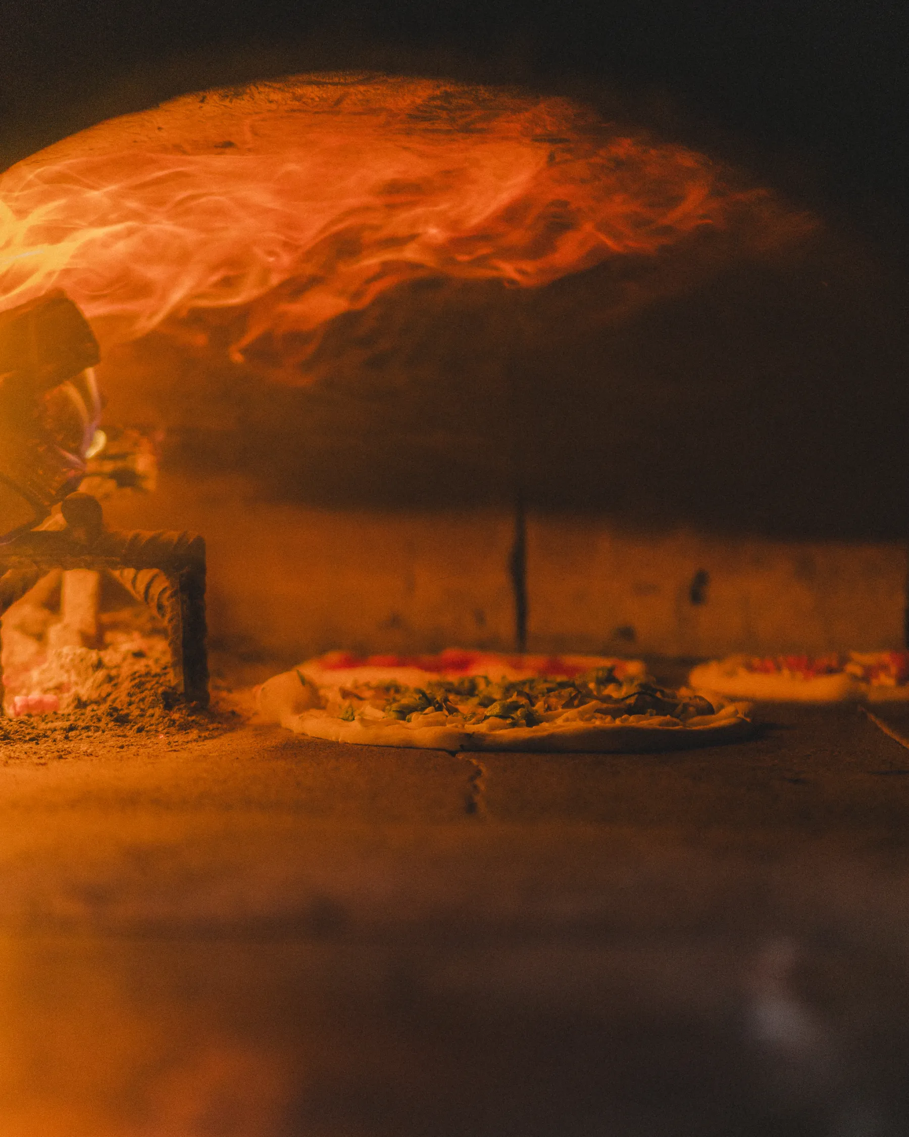 La pizza cuoce tra le fiamme del forno a legna